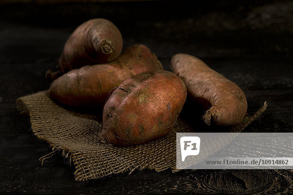 Vier Süßkartoffeln auf Jute und dunklem Holz
