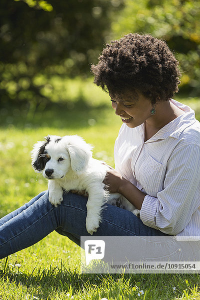 Junge Frau auf einer Wiese sitzend mit ihrem Hund auf dem Schoß