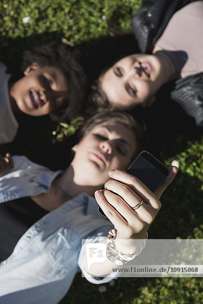 Three girl friends lying on grass taking selfie with smart phone