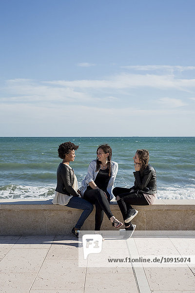 Drei junge Frauen  die am Meer sitzen und reden.