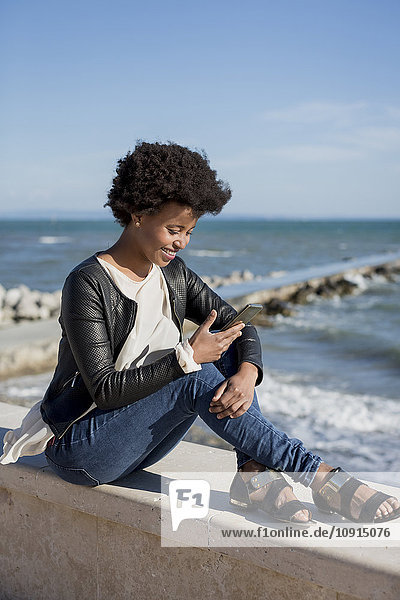 Young woman sitting by the sea  using smart phone