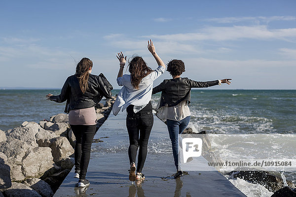 Three young women having fun on breakwater at the sea