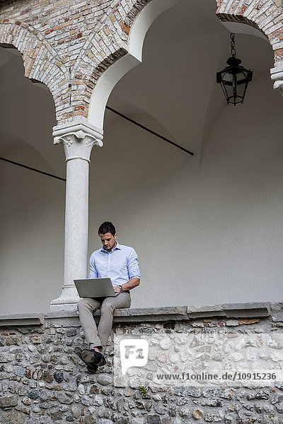 Geschäftsmann auf Steinmauer sitzend mit Laptop