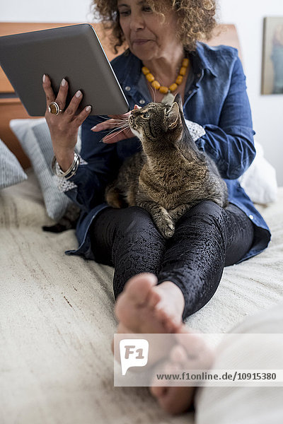 Woman with cat on bed holding digital tablet