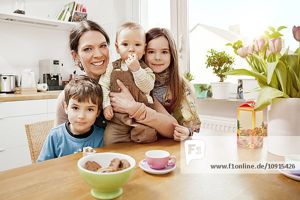 Porträt der glücklichen Mutter mit ihren drei kleinen Kindern in der Küche