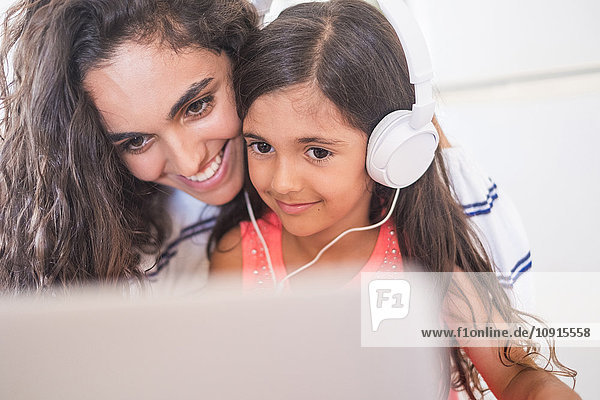 Happy teenage girl and her little sister with laptop and headphones
