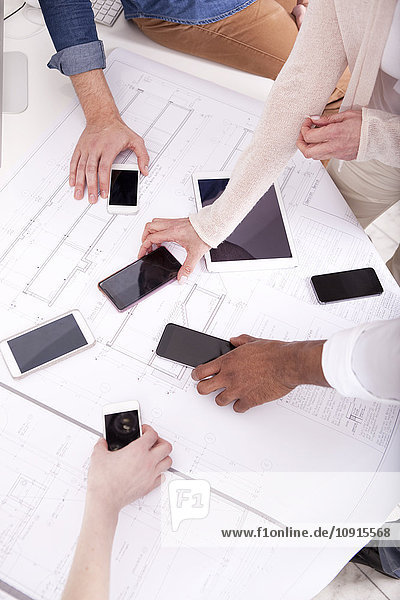 Hands taking smartphones lying on construction plan