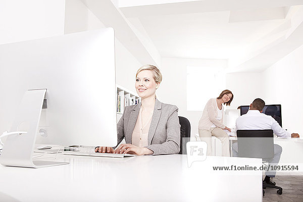 Geschäftsfrau  die am Schreibtisch im Büro arbeitet  während ihre Kollegen im Hintergrund reden.