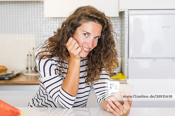 Porträt der lächelnden Frau mit Smartphone in der Küche