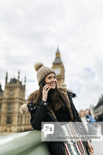 UK  London  happy young woman telephoning with smartphone in front of Palace of Westminster