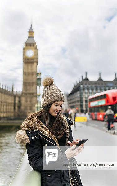 UK  London  smiling young woman looking at her smartphone in front of Palace of Westminster