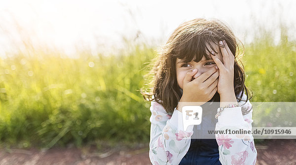 Porträt eines kleinen Mädchens  das den Mund mit der Hand bedeckt  während es etwas beobachtet.