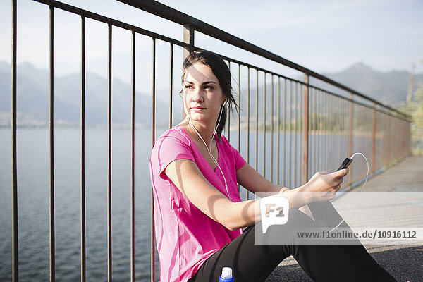 Italien  Lecco  sportliche junge Frau am Seeufer beim Musik hören