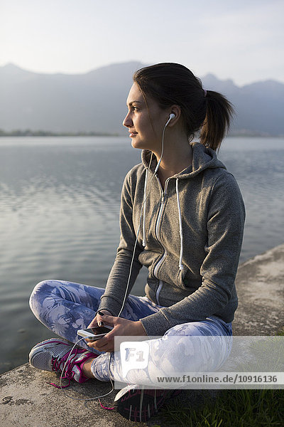 Italien  Lecco  entspannte junge Frau am Seeufer beim Musik hören