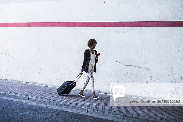 Gehende Geschäftsfrau mit Gepäck beim Blick auf ihr Smartphone