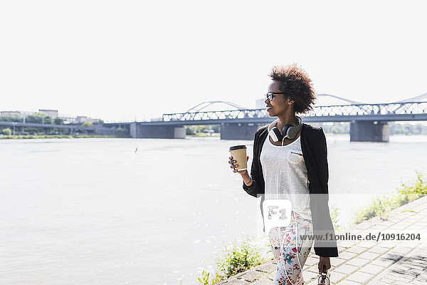 Deutschland  Mannheim  junge Geschäftsfrau mit Kaffee zum Spazierengehen am Flussufer