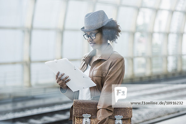 Junge Frau mit Aktentasche und Aktenlesung beim Warten am Bahnsteig
