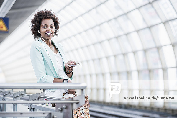 Porträt einer jungen Frau mit Kopfhörer und Smartphone am Bahnsteig