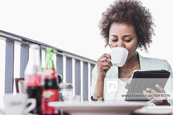 Junge Frau in einem Café  die Kaffee trinkt  während sie auf ihr digitales Tablett schaut.