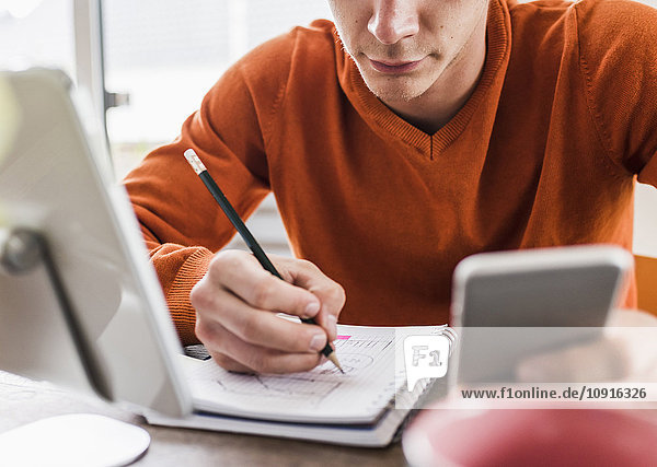 Mann am Schreibtisch mit Handy  digitalem Tablett und Notizblock