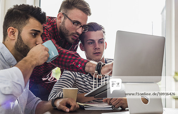 Three young professionals sharing laptop in office