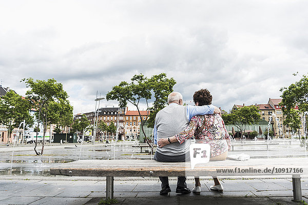 Deutschland  Mannheim  Rückansicht eines älteren Paares  das auf einer Bank sitzt und sich umarmt.