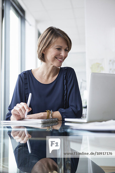 Lächelnde Geschäftsfrau bei der Arbeit am Laptop am Schreibtisch