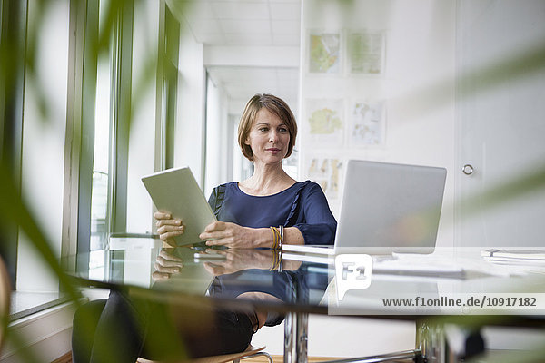 Geschäftsfrau mit digitalem Tablett und Laptop am Bürotisch