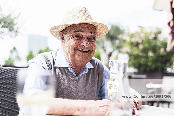 Porträt eines glücklichen älteren Mannes  der in einem Straßencafé ein Glas Bier trinkt.