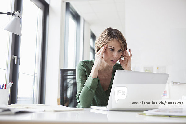 Konzentrierte Geschäftsfrau bei der Arbeit am Laptop am Schreibtisch