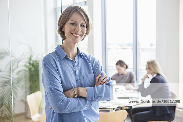 Porträt einer lächelnden Geschäftsfrau mit Kollegen im Hintergrund