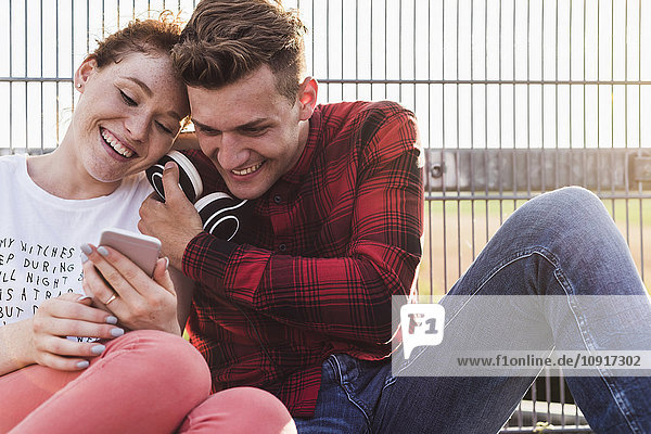 Smiling young couple at a fence with headphones and smartphone