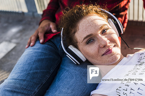 Junge Frau mit Kopfhörer auf dem Schoß des Freundes liegend