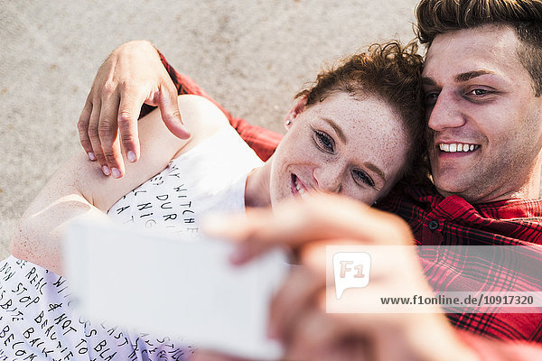 Lächelndes junges Paar im Liegen mit einem Selfie