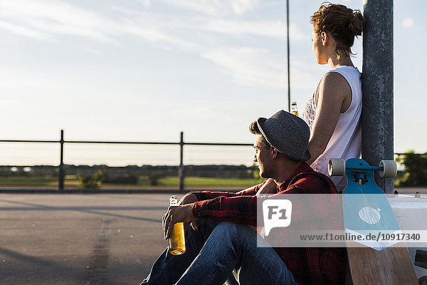 Young couple with skateboard and beer bottle enjoying the sunset
