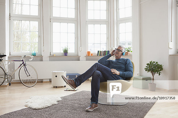 Entspannter reifer Mann zu Hause im Sessel sitzen und Musik hören