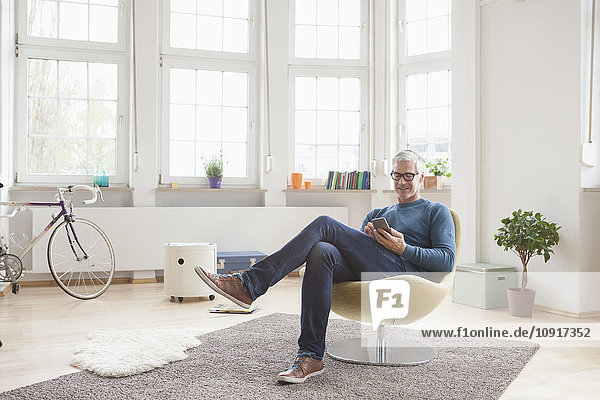 Erwachsener Mann zu Hause im Sessel sitzend mit digitalem Tablett