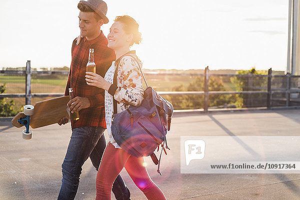 Young couple with beer bottles and skateboard at sunset