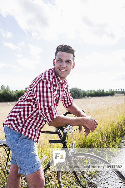 Lächelnder junger Mann mit Fahrrad in der Natur