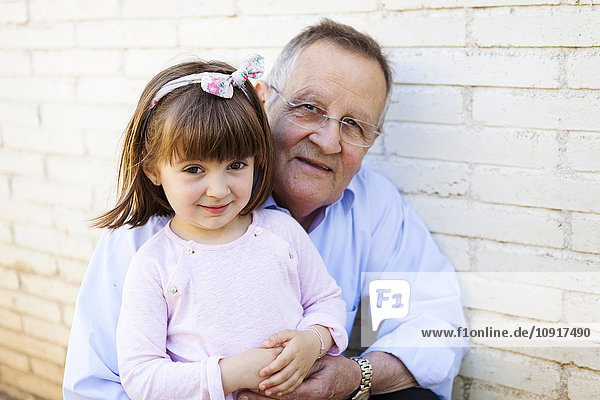 Portrait of grandfather with his little granddaughter in front of white brick wall