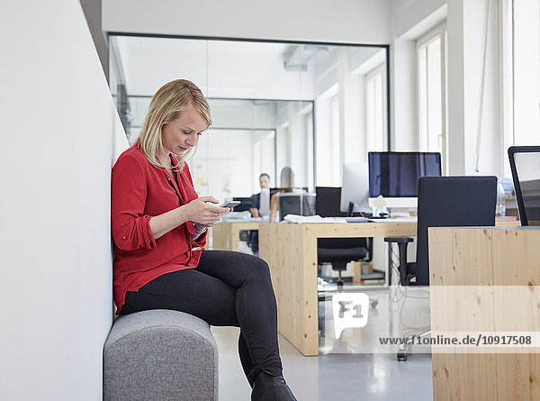 Frau im Büro sitzend mit Smartphone