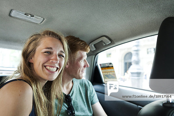 Porträt einer grinsenden Frau im Taxi mit ihrem Freund im Hintergrund