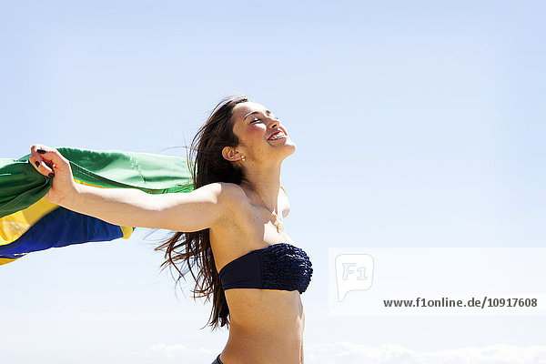 Junge brünette Frau spielt mit brasilianischer Flagge am Strand