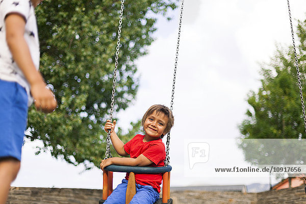 Porträt eines glücklichen kleinen Jungen  der auf einer Schaukel sitzt.