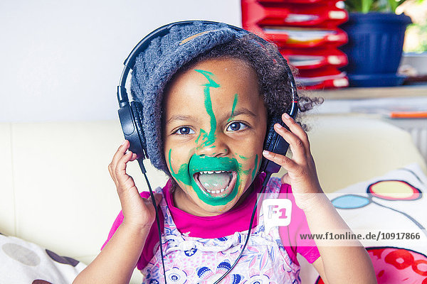 Porträt eines glücklichen kleinen Mädchens mit gemaltem Gesicht  das Musik mit Kopfhörern hört.