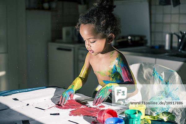 Mädchen zeichnet rotes Bild mit Fingerfarben und ist voll von Farben verschmiert