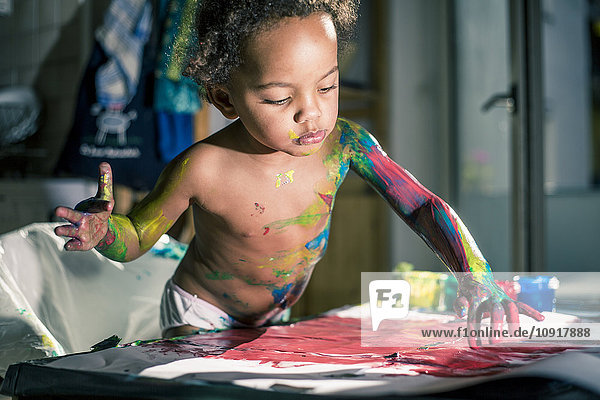Mädchen zeichnet rotes Bild mit Fingerfarben und ist voll von Farben verschmiert