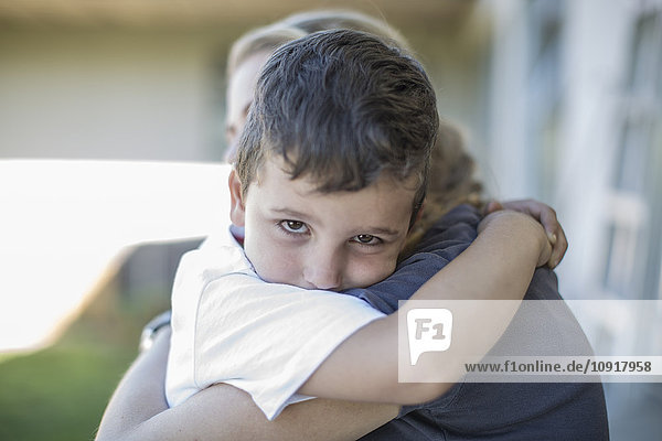 Porträt eines traurigen kleinen Jungen,  der seine Mutter umarmt.
