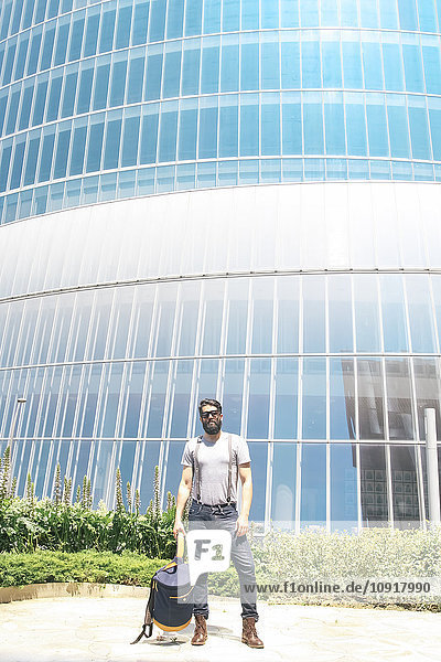 Mann mit Sonnenbrille  der vor einem modernen Gebäude steht.