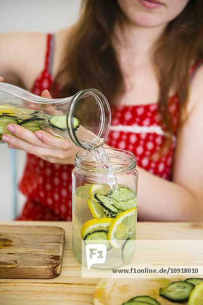 Woman pouring detox water infused with lemon and cucumber into a glass